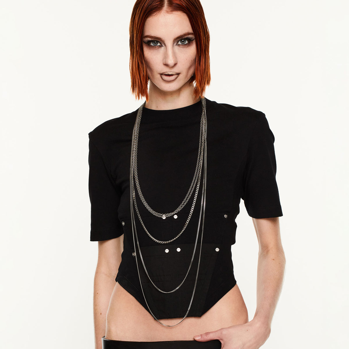 Woman wearing a black outfit with layered necklaces on a white background