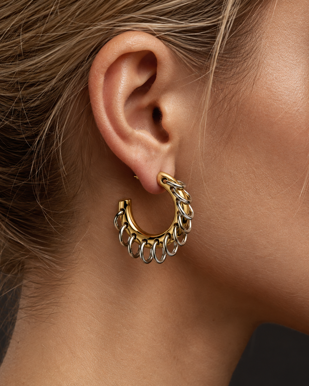 A close-up of a model's ear wearing a gold hoop earring with a textured, chain-like twisted design.