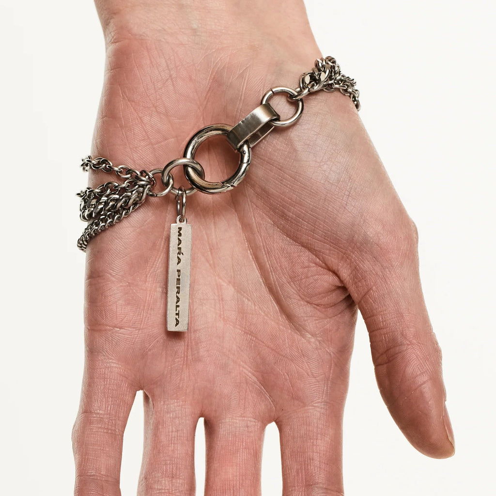 Hand wearing a silver bracelet with charms on a plain background